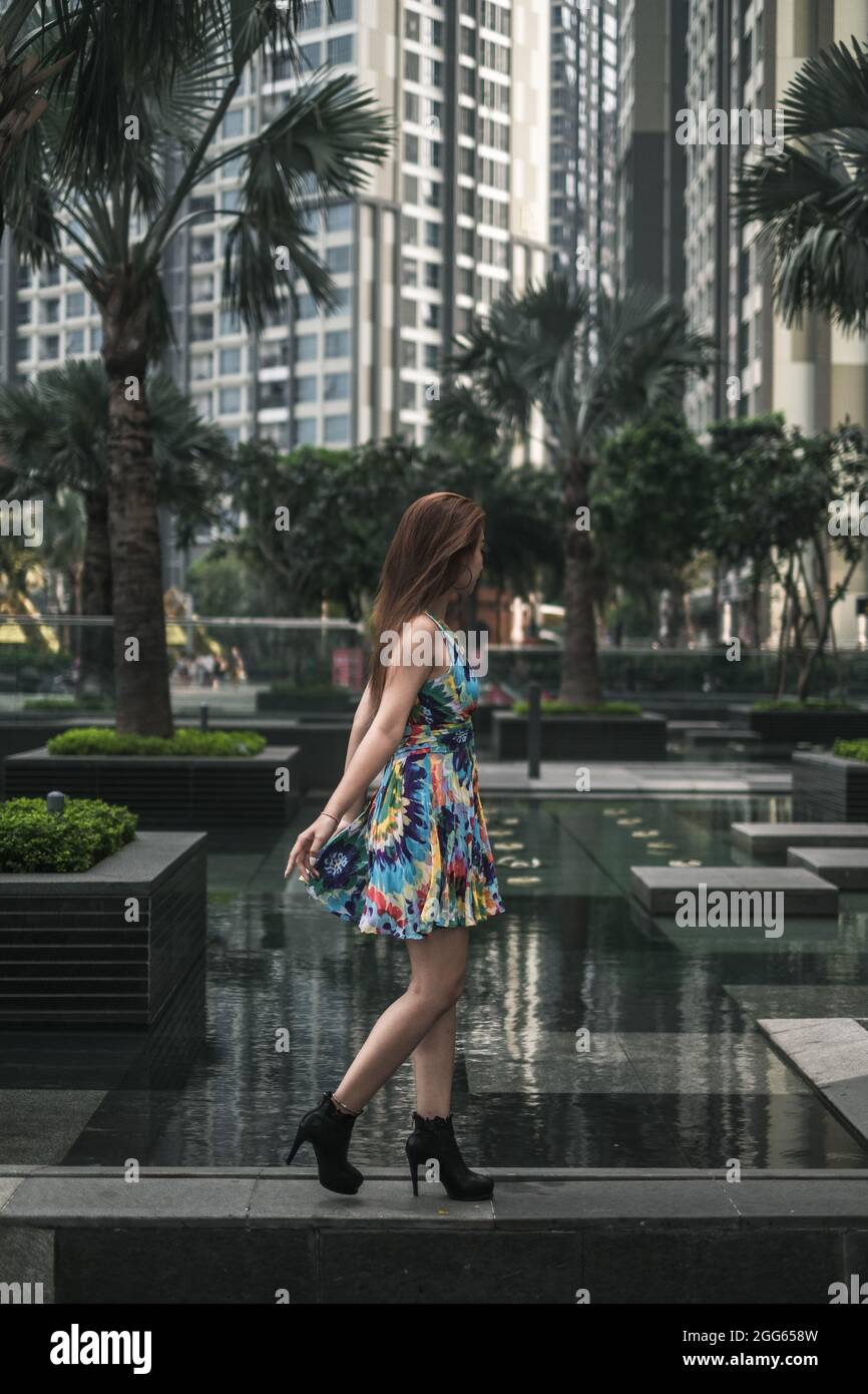 Hübsche asiatische Frau in lässigen bunten Kleid zu Fuß im Freien in der Metropole. Langes Haar. Schöne Haltung. Hochwertige Fotos Stockfoto