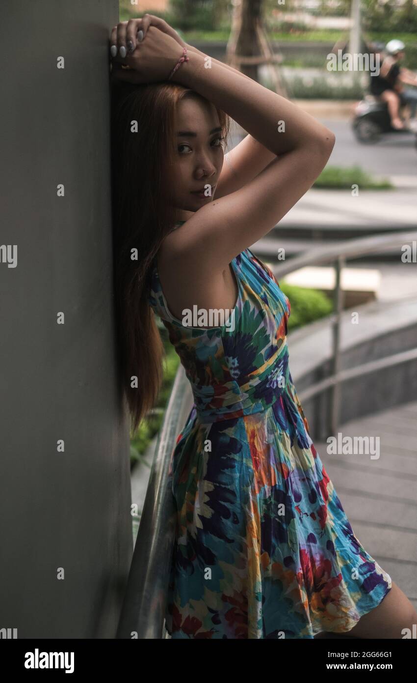 Schöne asiatische junge Frau in lässigen bunten Kleid im Freien stehen. Die Hände hoch halten. Langes Haar. Schöne Haltung. Hochwertige Fotos Stockfoto