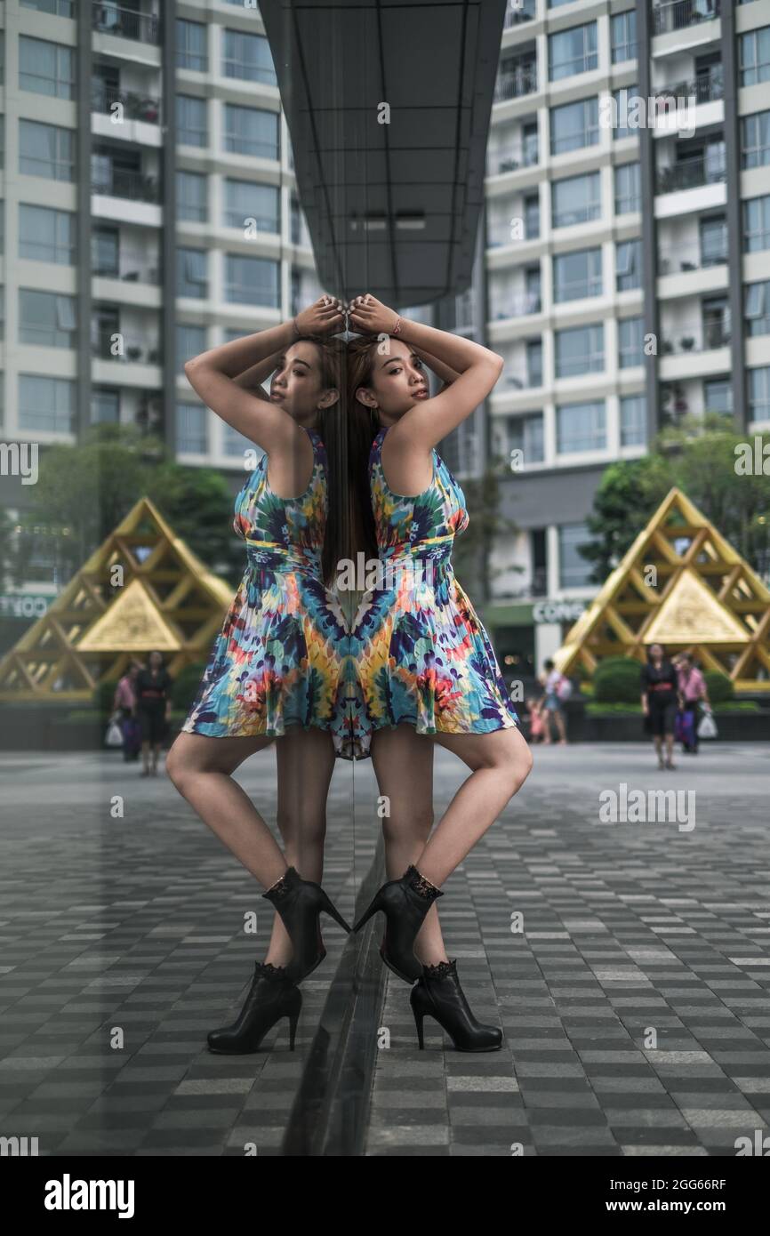 Schöne asiatische Frau in lässigen bunten Kleid steht im Freien in der Nähe des modernen Gebäudes. Langes Haar. Schöne Haltung. Hochwertige Fotos Stockfoto