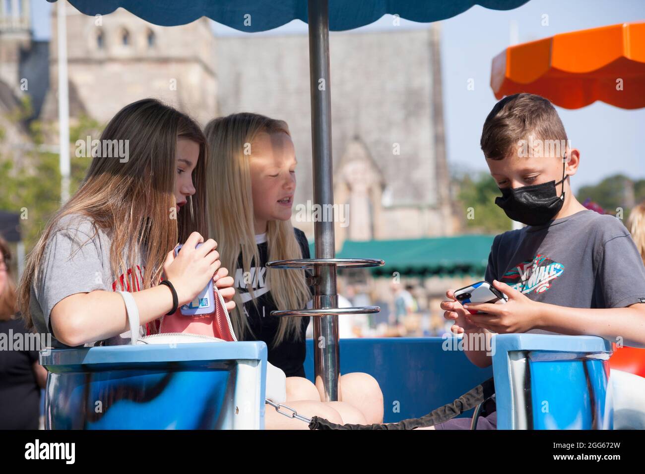 Jugendliche auf der Teetailfahrt beim Sommerfayre in Helensburgh, Schottland, mit Mobiltelefonen und in einer Maske. Stockfoto