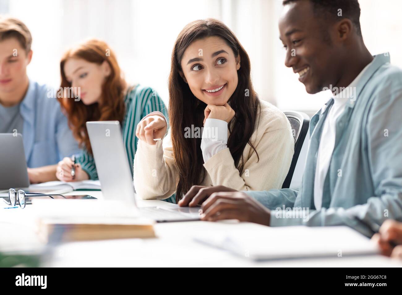 Lächelnde Studenten, die am Schreibtisch sitzen und an einem Gruppenprojekt arbeiten Stockfoto