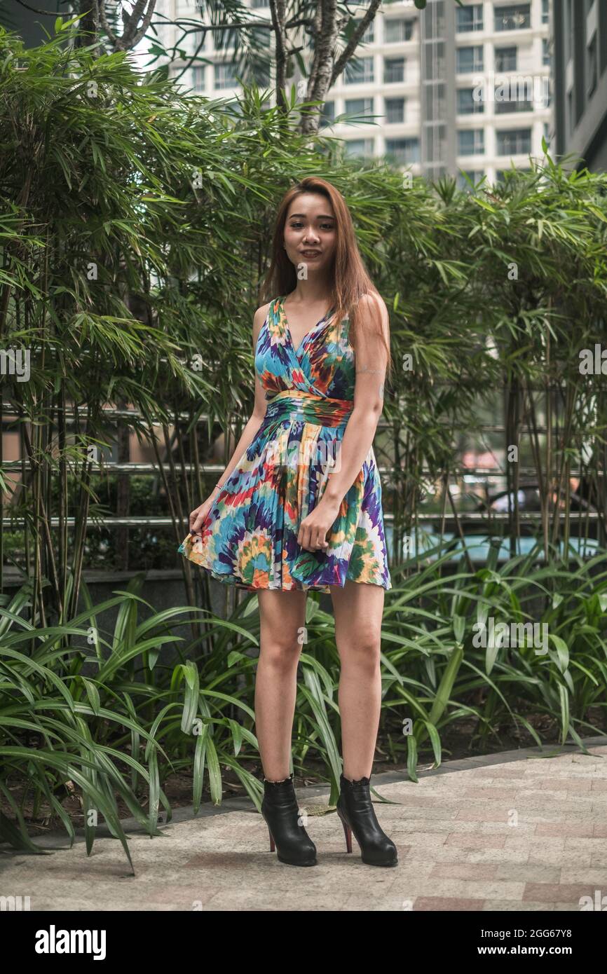 Hübsche junge asiatische Frau in lässigem, farbenfrohem Kleid, die im Park steht und lächelt. Langes Haar. Schöne Haltung. Hochwertige Fotos Stockfoto