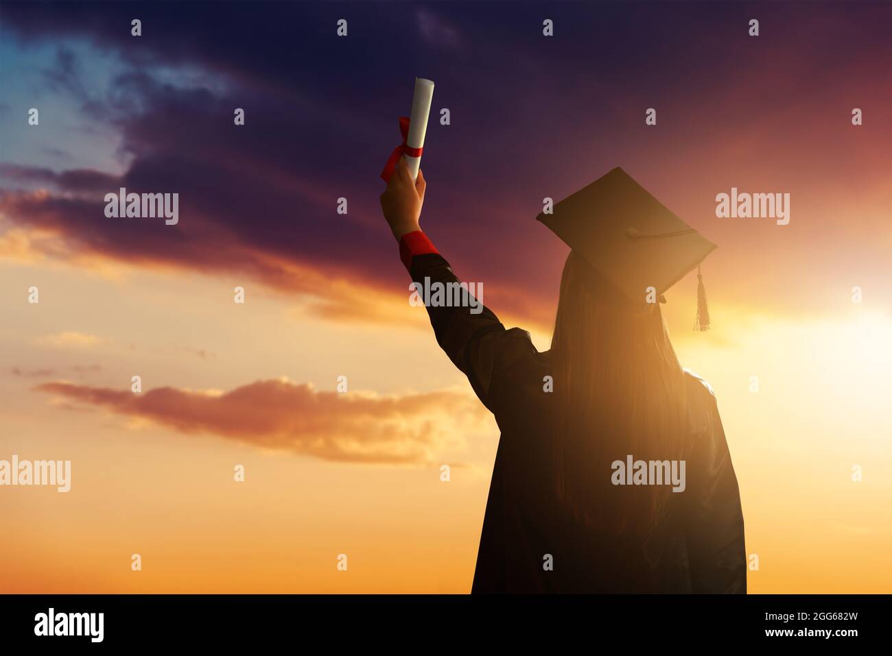 Eine hübsche Studentin, die ihren Abschluss feiert und sich gegen den idyllischen Sonnenuntergang stellt und ihr Diplom hoch hält. Hochwertige Fotos Stockfoto