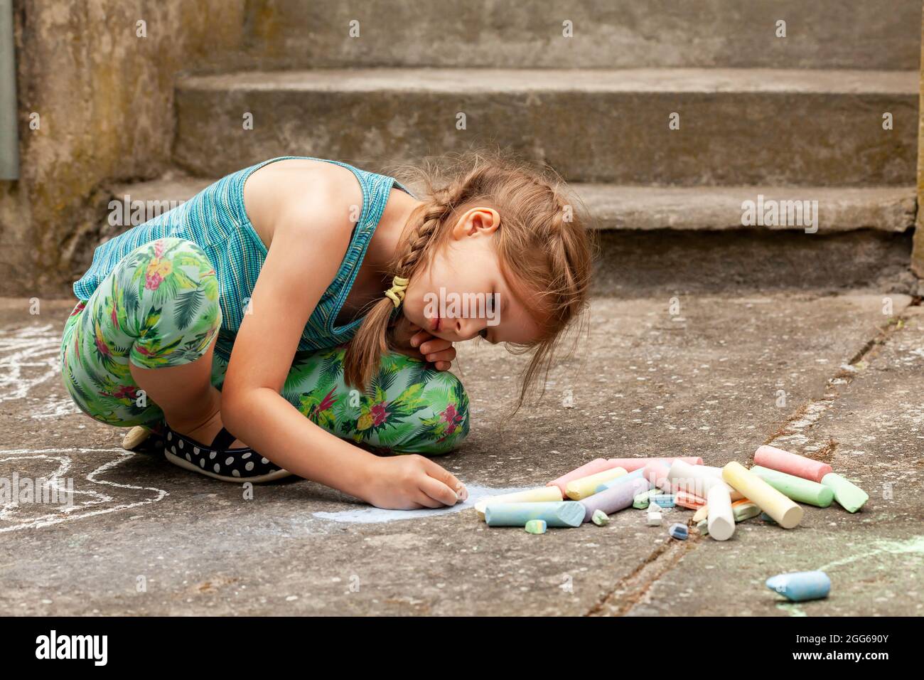 Kleines Kind im Schulalter, das mit Kreide auf dem Beton auf dem Boden sitzt. Kunsttherapie, sensorische Integration einfaches Konzept. Kreative Arti Stockfoto