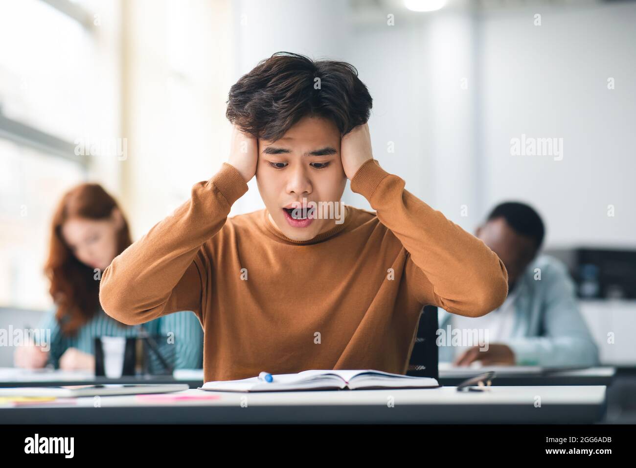 Schockiert asiatische Student Grabbing Kopf sitzen am Schreibtisch in der Klasse Stockfoto