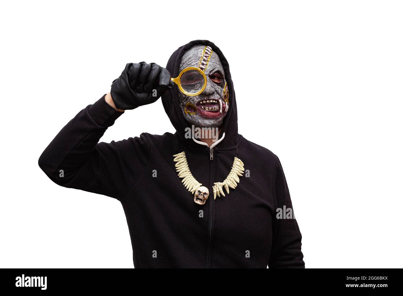 Ein Mann, der in einer Zombie-Maske verkleidet ist und in einem schwarzen Kapuzen-Sweatshirt gekleidet ist, schaut durch eine Lupe. Stockfoto