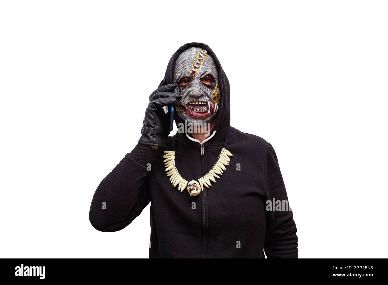 Ein Mann, der in einer Zombie-Maske verkleidet ist und in einem schwarzen Kapuzen-Sweatshirt gekleidet ist, telefoniert mit seinem Smartphone. Stockfoto