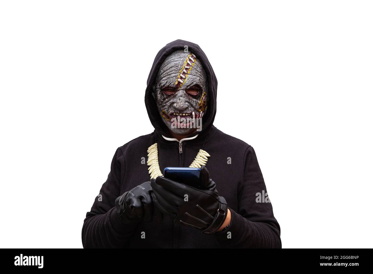 Ein Mann, der in einer Zombie-Maske verkleidet ist und ein schwarzes Kapuzen-Sweatshirt trägt, berührt den Touchscreen eines Mobiltelefons. Stockfoto