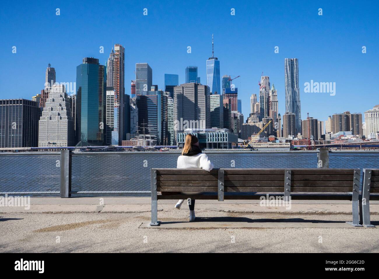 Junge Frau, die irgendwo in brooklyn auf einer öffentlichen Bank sitzt. Blick auf Manhattan in New York City. Stadtbild. Das Leben in der Großstadt Stockfoto