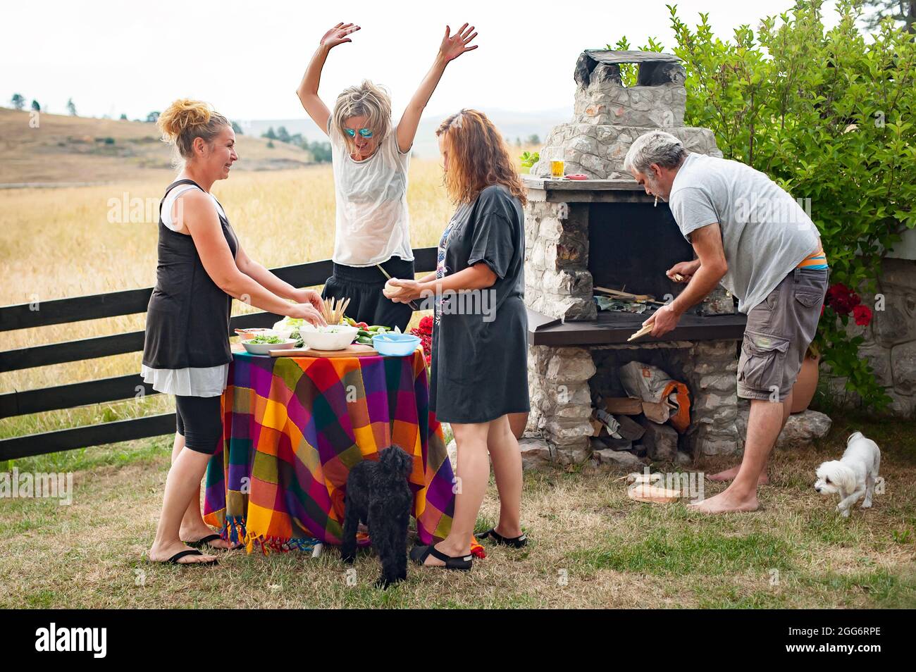 Fröhliche und verspielte Freunde lachen, tanzen und genießen das Bergambiente und grillen vor ihrem Haus Stockfoto