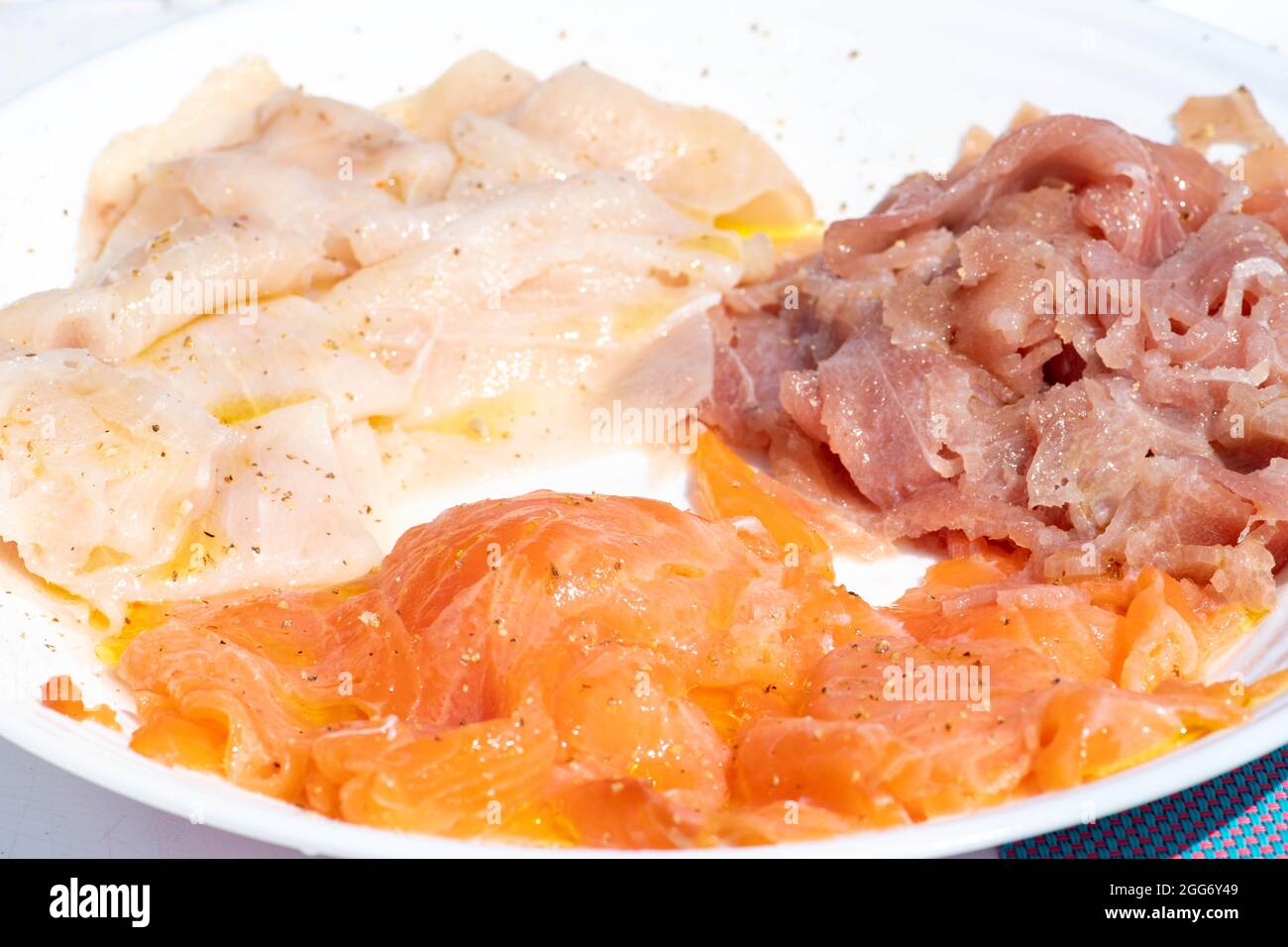 Platte mit köstlichem Carpacio mit frischem Schwertfisch, Lachs und Thunfisch, gewürzt mit nativem Olivenöl extra, Pfeffer und Zitronensaft, Sushi Stockfoto