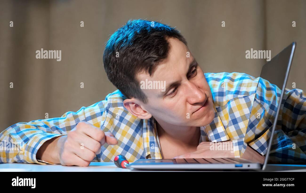 Junger Mann klopft an Laptop und wird wütend Stockfoto