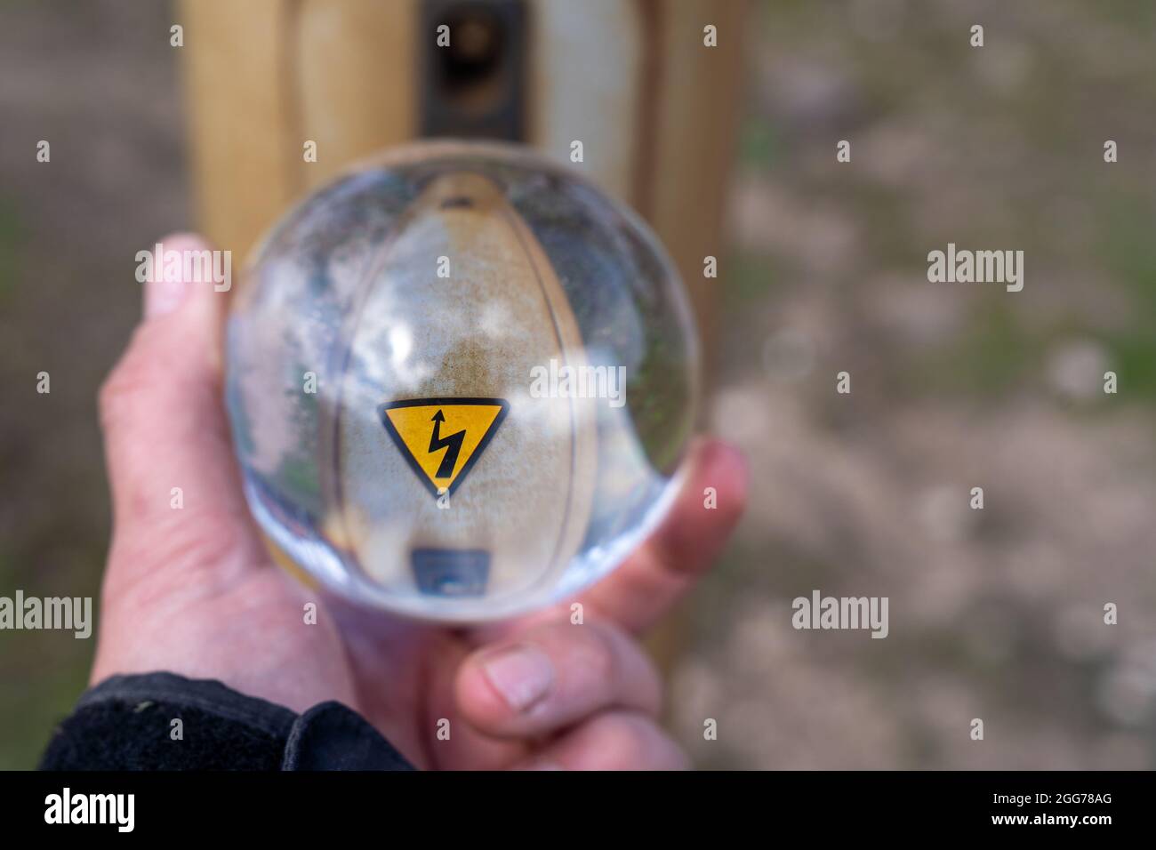 Das Blitzsymbol Blitz auf einem gelben dreieckigen Hintergrund ist durch eine Glaskugel in der Hand sichtbar. Das schwarze Blitzsymbol auf einem Ye Stockfoto