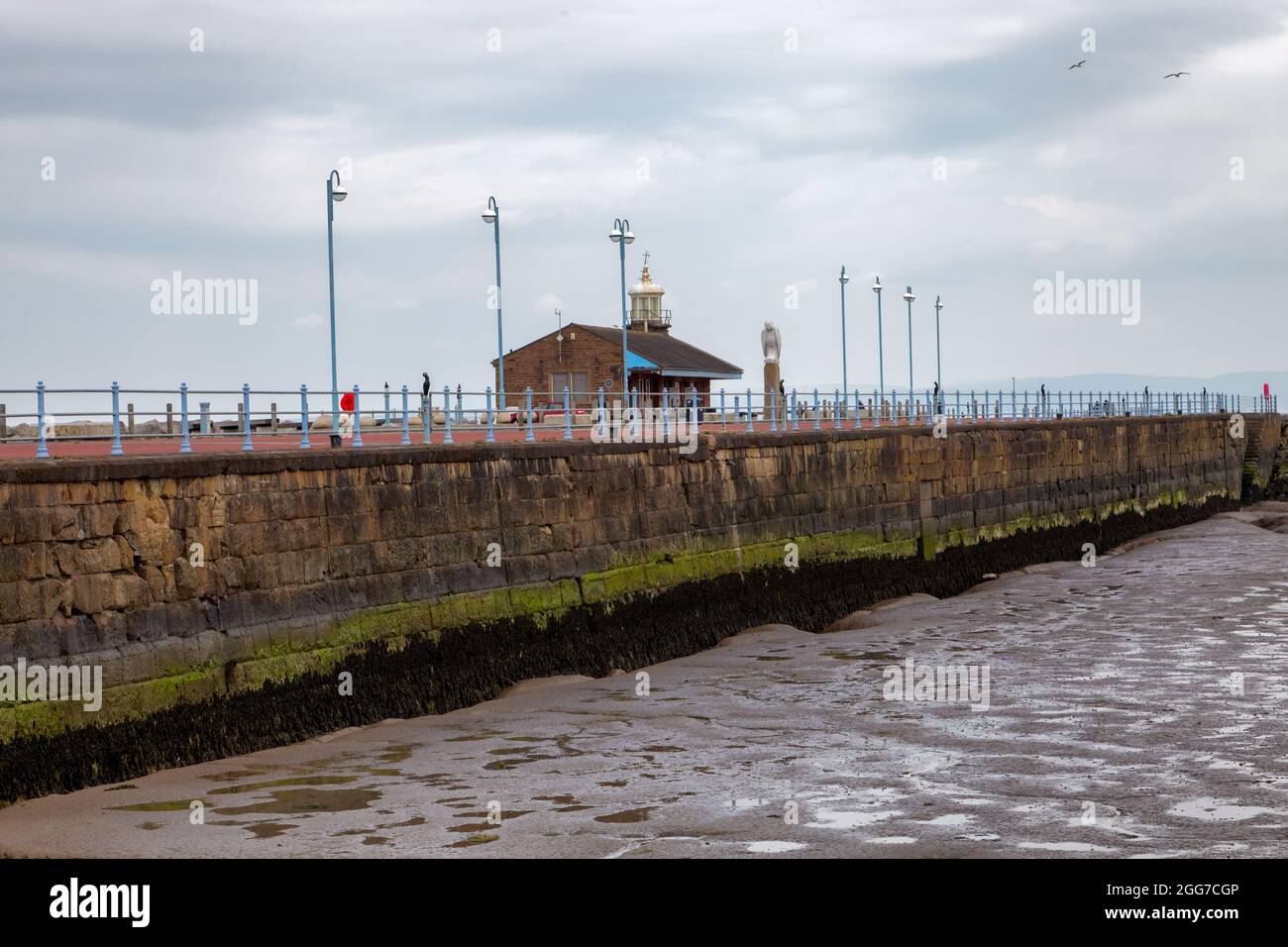 Die Steinerne Anlegestelle bei Morecambe bei Ebbe. Ein kleiner Leuchtturm liegt neben dem stillstehenden Bahnhofsgebäude Stockfoto