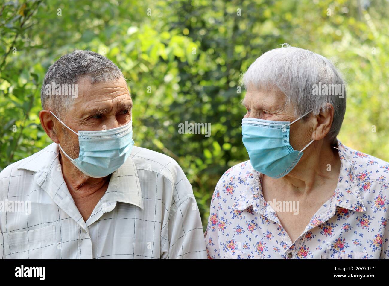 Ältere Paare in schützenden Gesichtsmasken, die sich auf dem Hintergrund der Natur anblicken. Sicherheit während einer Coronavirus-Pandemie, Leben im Ruhestand Stockfoto
