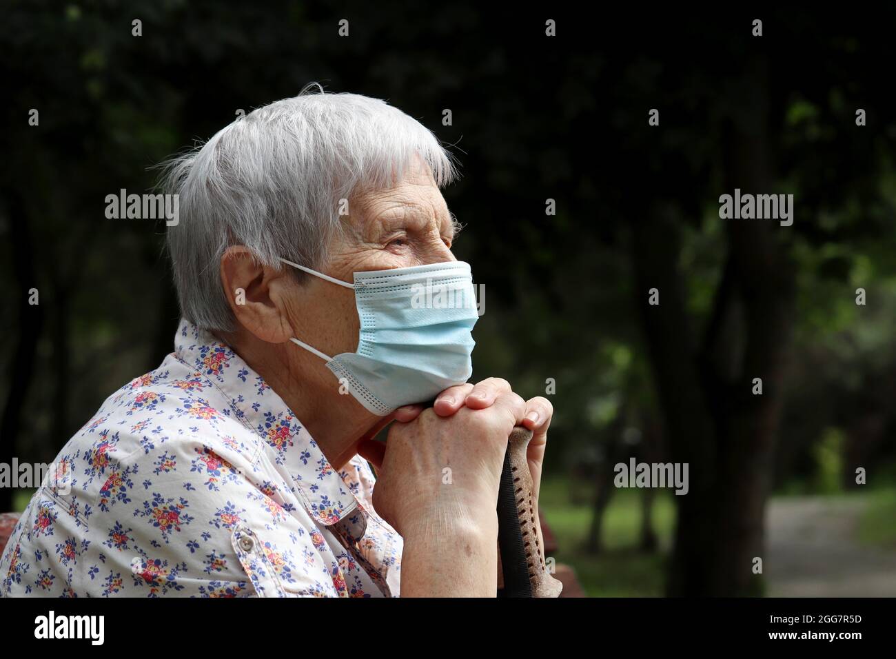 Alte Frau in Schutzmaske sitzt auf einer Bank im Park. Sicherheit während einer Coronavirus-Pandemie, Leben im Ruhestand Stockfoto