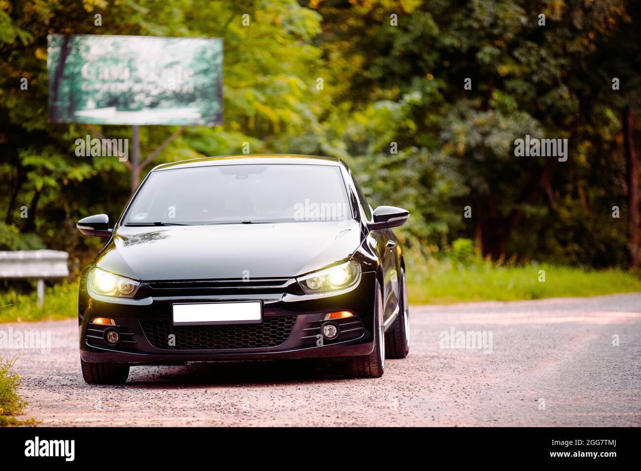 Die schwarz schöne glänzende Autolimousine fährt auf der Straße im Wald ohne Nummer und mit eingeschalteten Scheinwerfern. Stockfoto