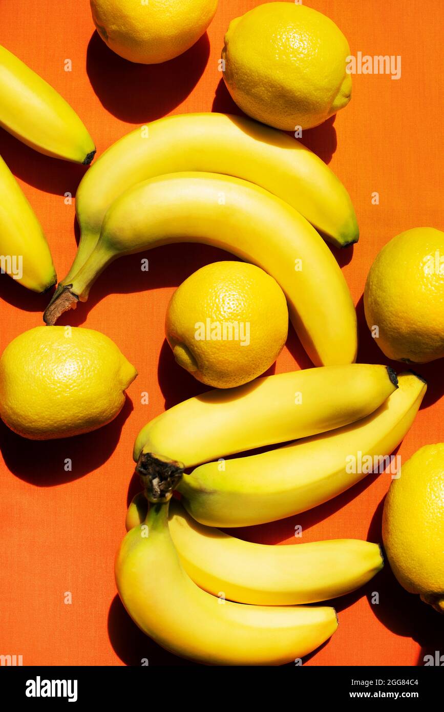 Overhead-Ansicht von Bananen und Zitronen auf orangefarbenem Hintergrund Stockfoto