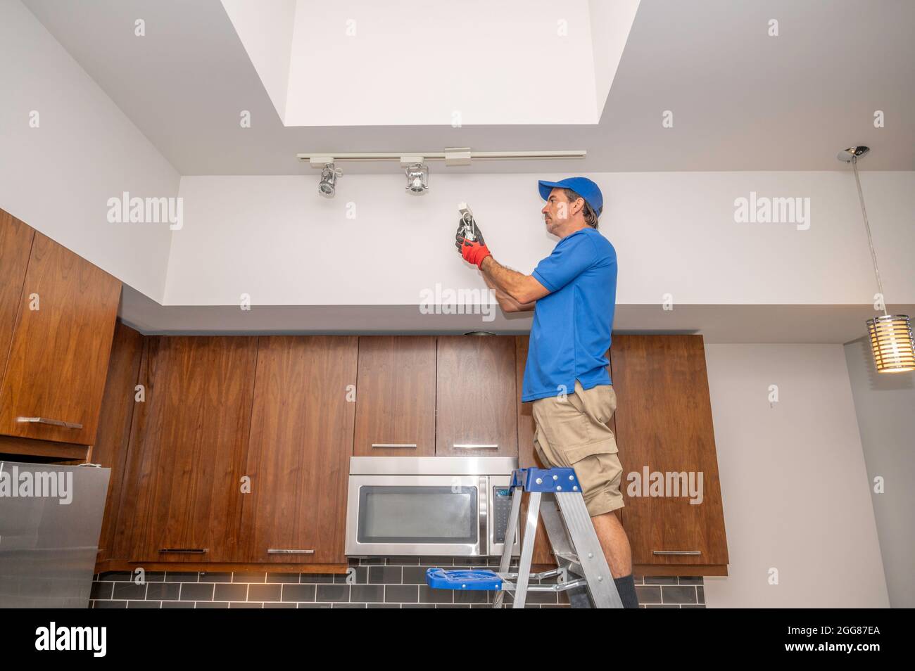 Elektriker, der auf einer Leiter steht und eine Leuchte an der Gleisbeleuchtung auswechselt Stockfoto