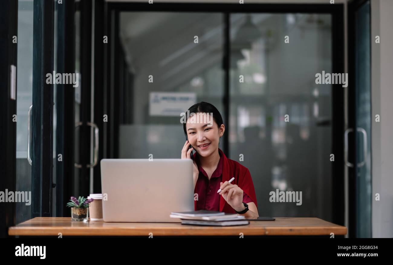Portrait junge asiatische Geschäftsfrau schöne charmante lächeln und sprechen auf dem Handy im Büro. Weibliche Arbeit mit Laptop-Computer Stockfoto