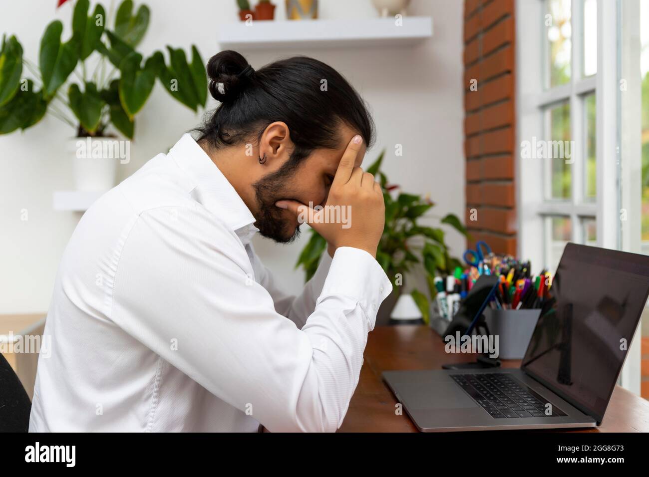 Frustrierter junger Mann mit langen Haaren vor einem Laptop. Stockfoto