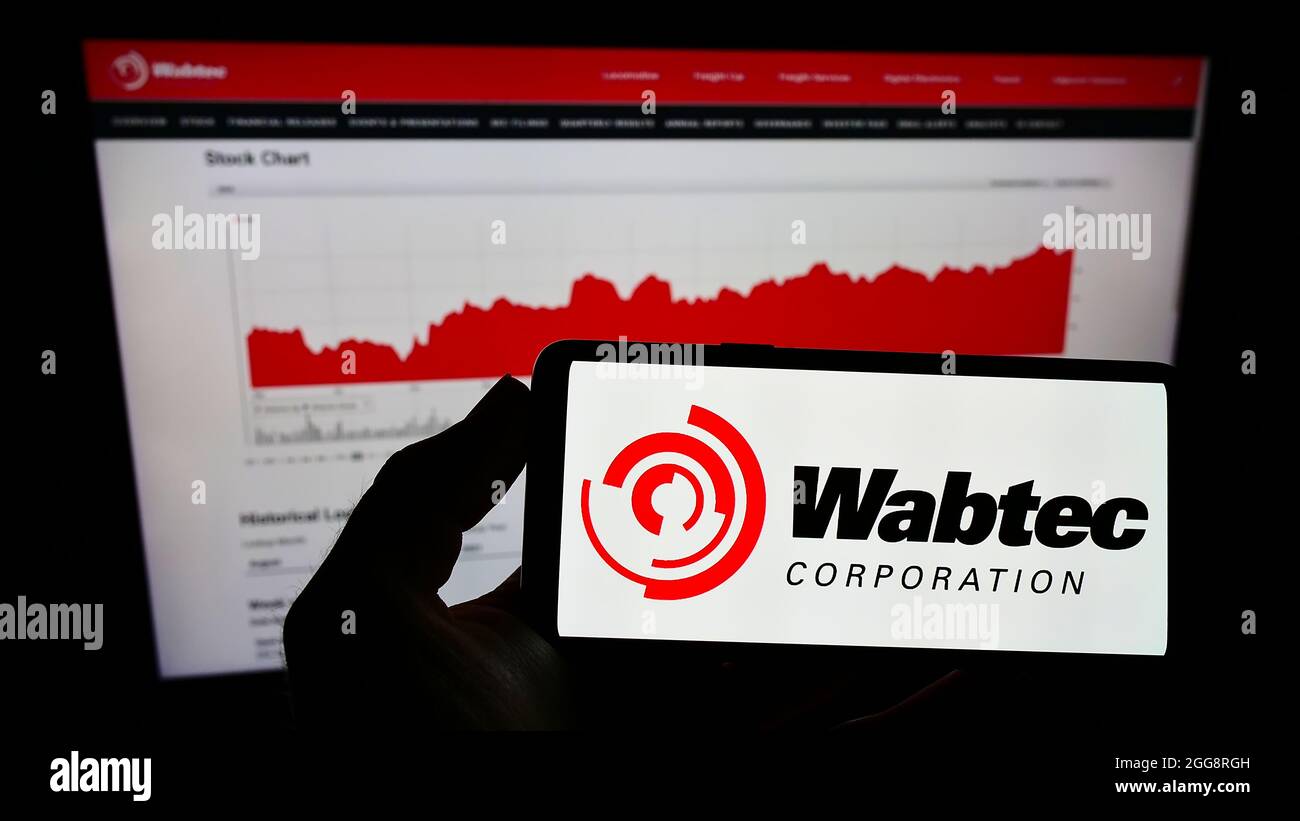 Person, die das Mobiltelefon mit dem Logo des amerikanischen Eisenbahnherstellers Wabtec Corporation auf dem Bildschirm vor der Webseite hält. Konzentrieren Sie sich auf die Telefonanzeige. Stockfoto