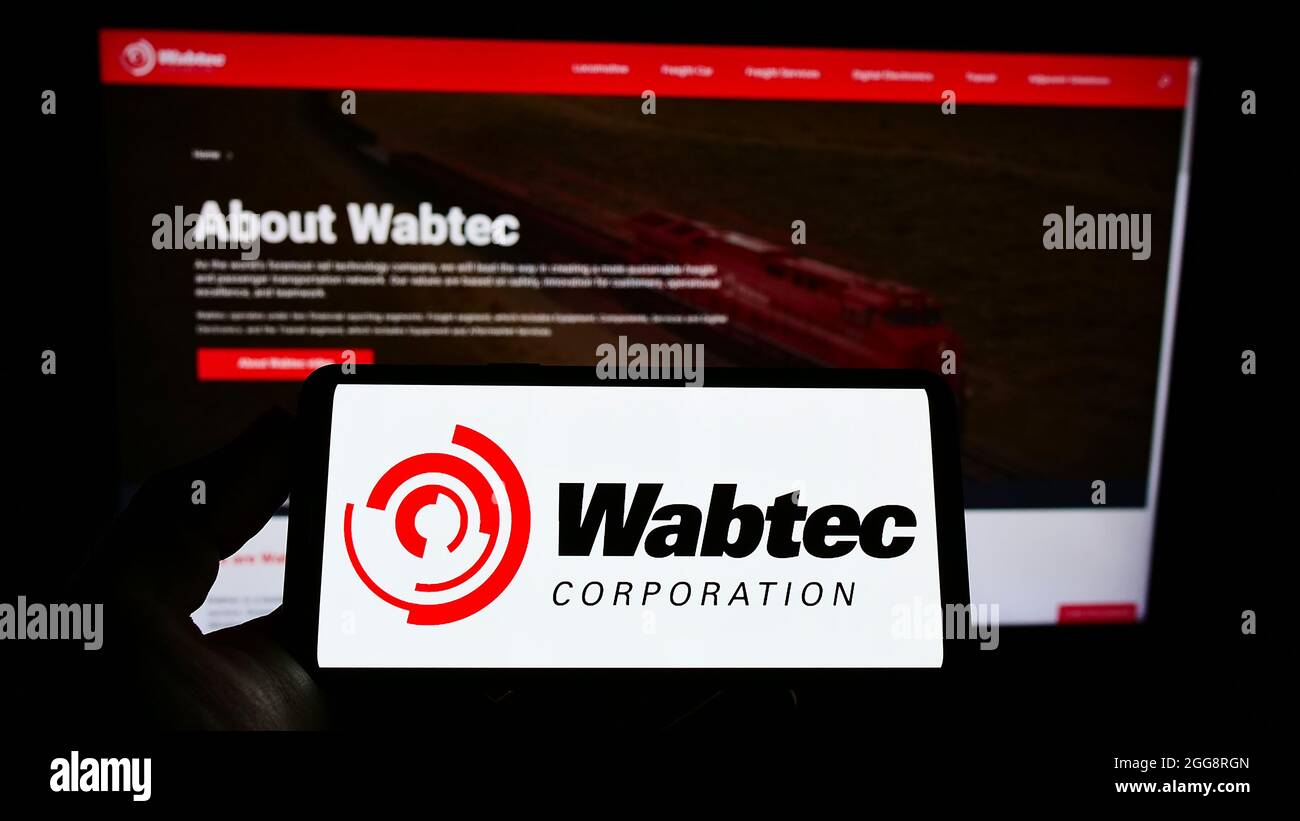 Person, die das Smartphone mit dem Logo des US-Eisenbahnherstellers Wabtec Corporation auf dem Bildschirm vor der Website hält. Konzentrieren Sie sich auf die Telefonanzeige. Stockfoto