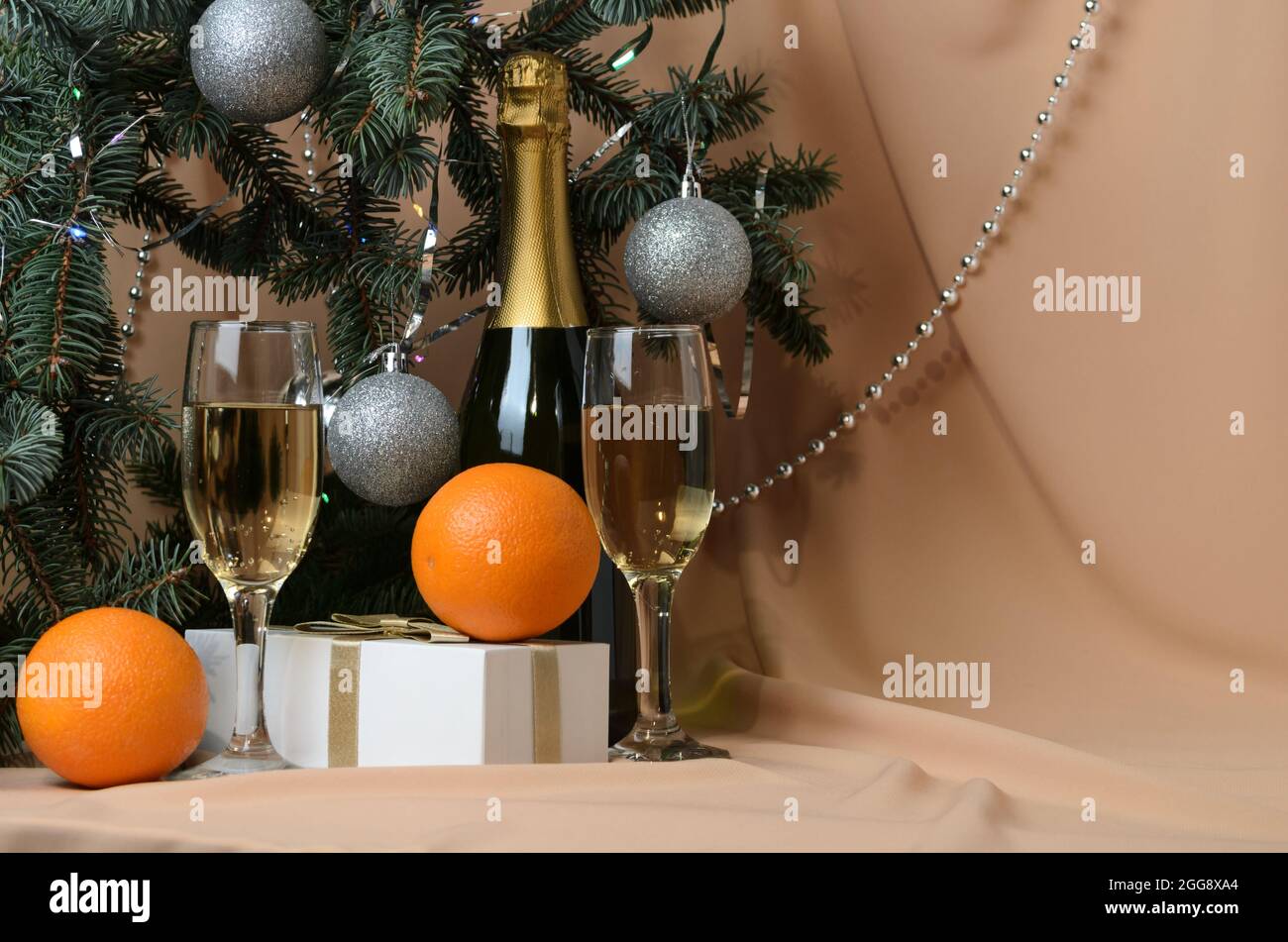 Eine Neujahrskomposition aus Zweigen eines Weihnachtsbaums, verziert mit silbernen Kugeln, einer Geschenkbox, Sektgläsern, Orangen auf einem Hintergrund Stockfoto