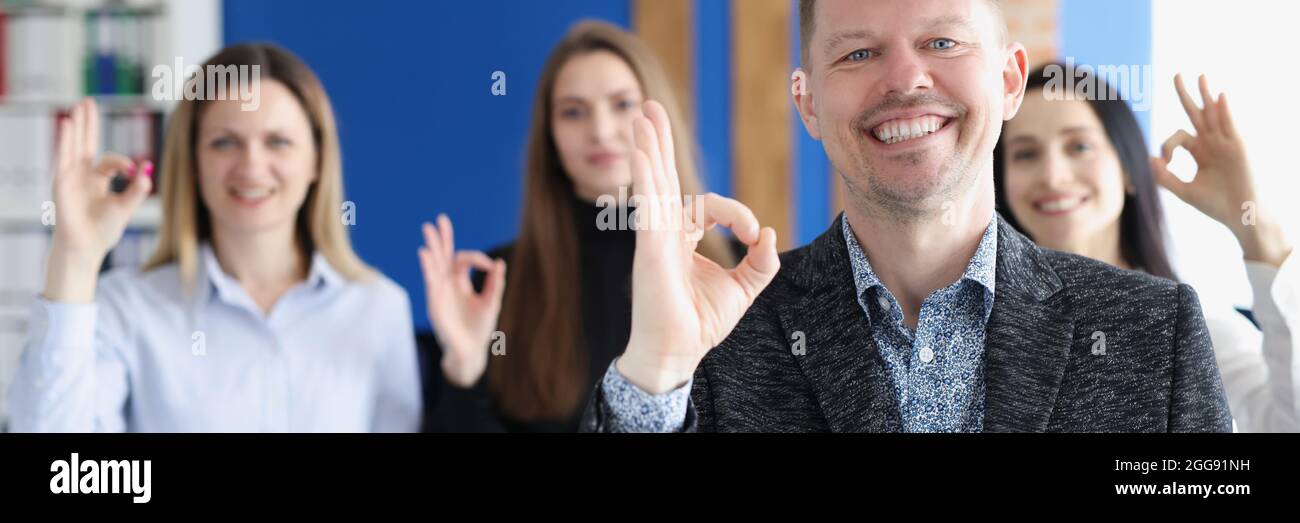 Geschäftsmann zeigt auf dem Hintergrund der Kollegen im Büro eine gute Geste Stockfoto