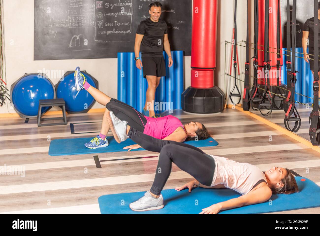 Frauen, die im Fitnessstudio mit einem Bein nach oben und einem Trainer trainieren Stockfoto