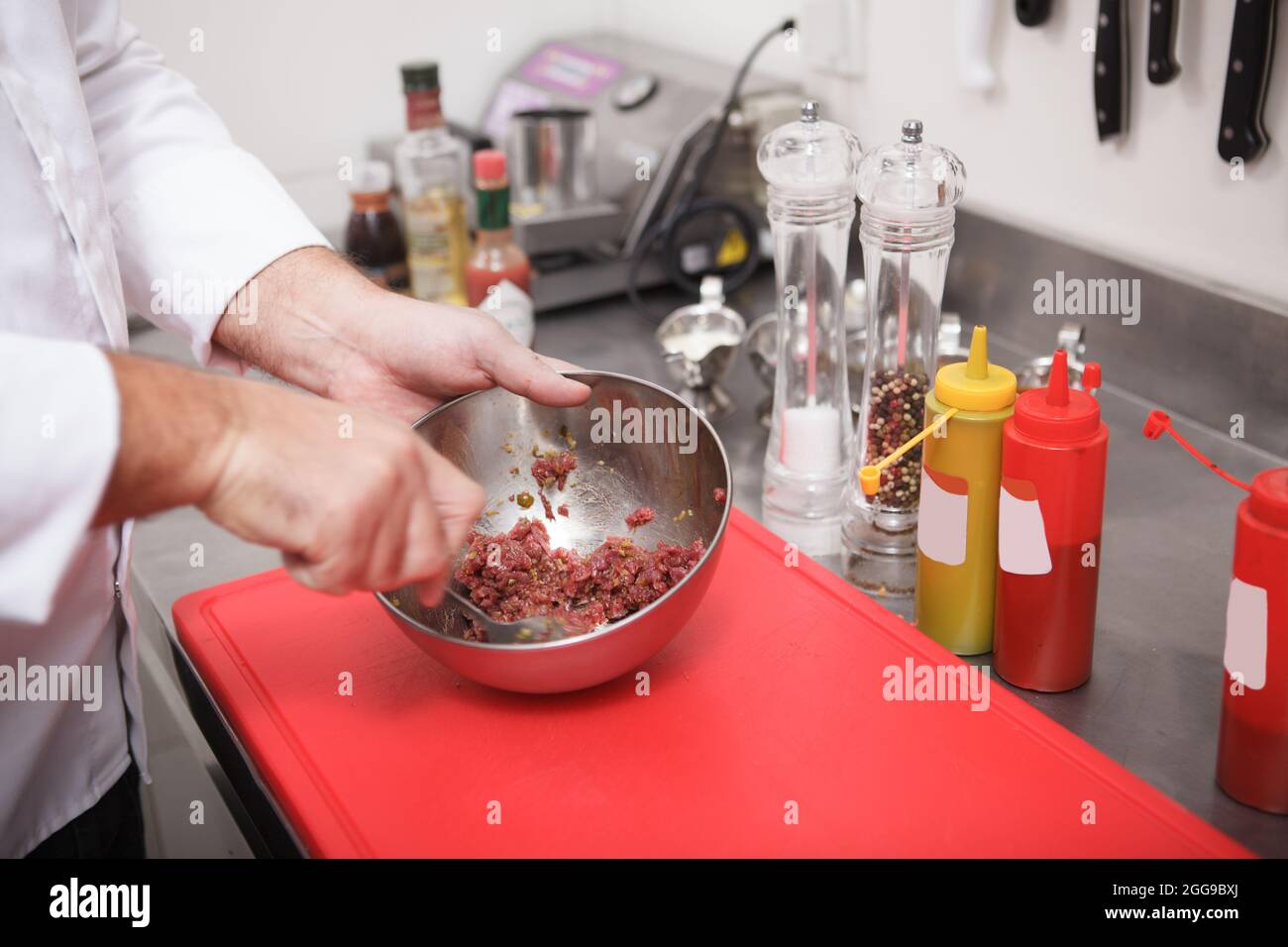 Nahaufnahme der Hände des Küchenchefs, die in einer Metallschüssel gehacktes Rindfleisch für Tartar rühren Stockfoto