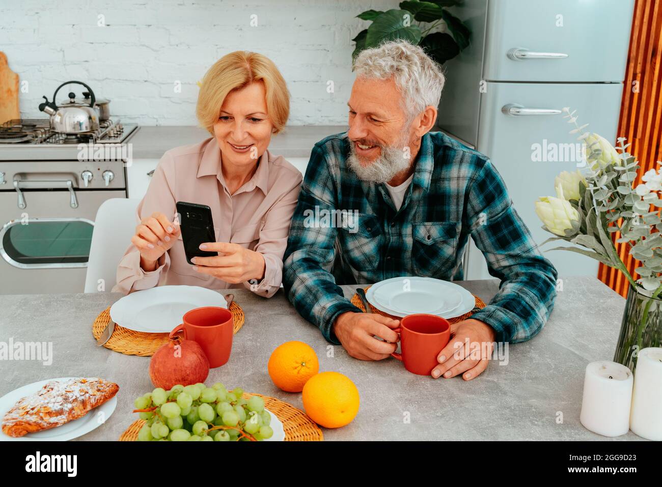 Das Paar frühstückt zu Hause und liest etwas vom Smartphone Stockfoto