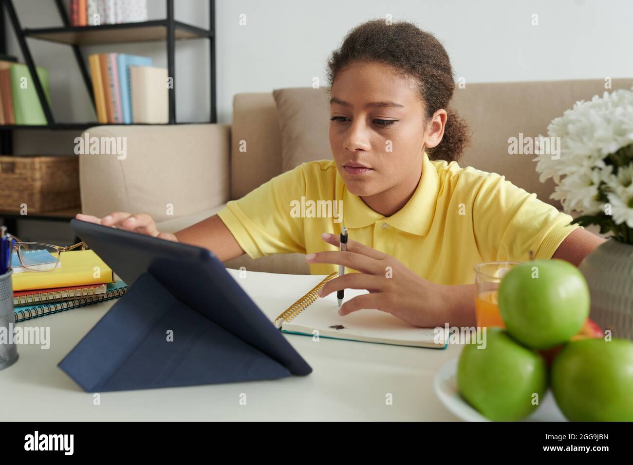 Ernsthaftes Teenager-Mädchen, das Online-Kurs besucht, Videos auf einem Tablet-Computer ansieht und sich Notizen zu Lehrbüchern macht Stockfoto