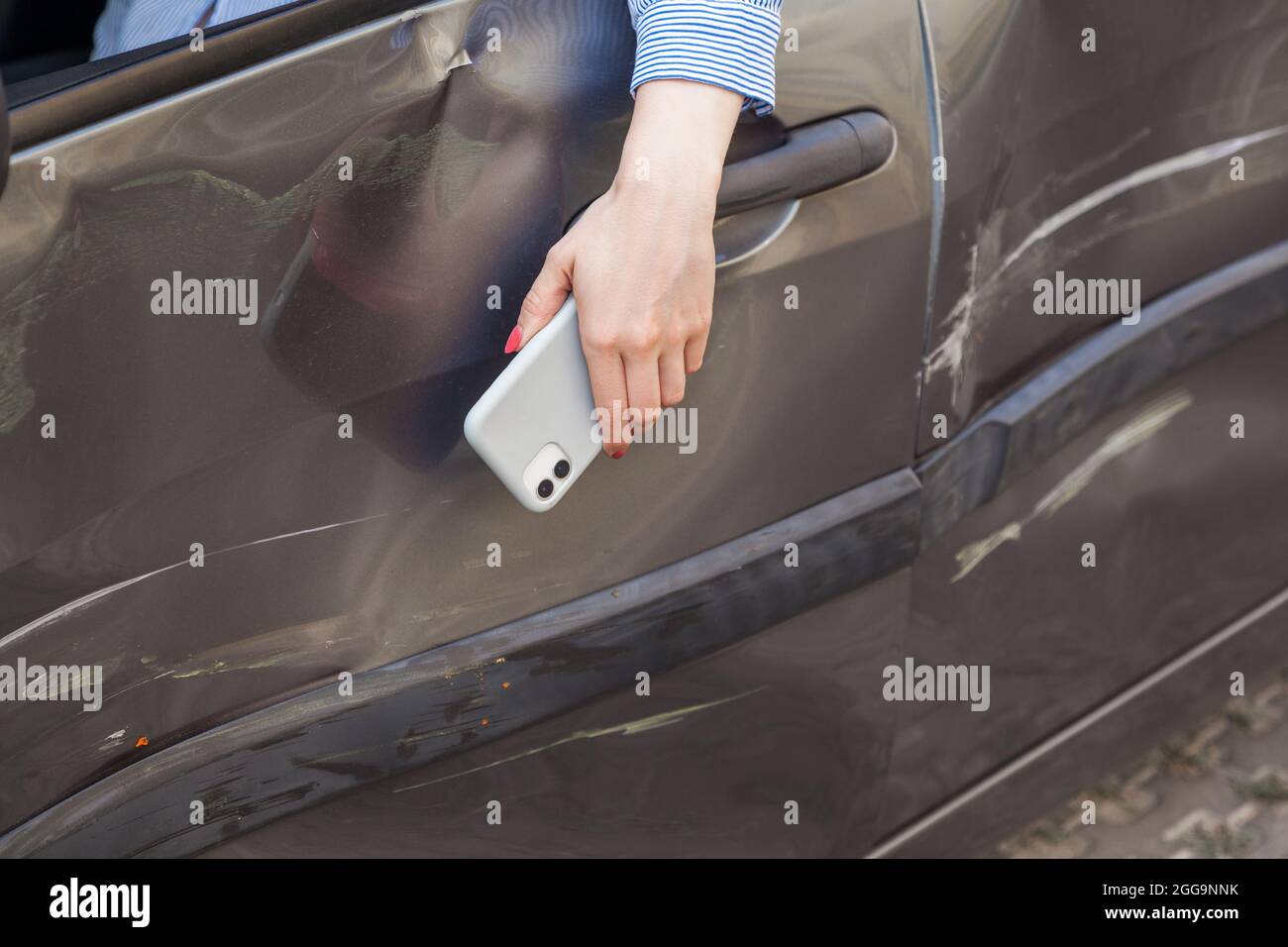 Nahaufnahme einer Frauenhand mit Mobiltelefon, das am Autofenster hängt, betrunkener Fahrer in einem beschädigten Auto, verletzte Frau im Auto mit Beulen und kratzresten Stockfoto