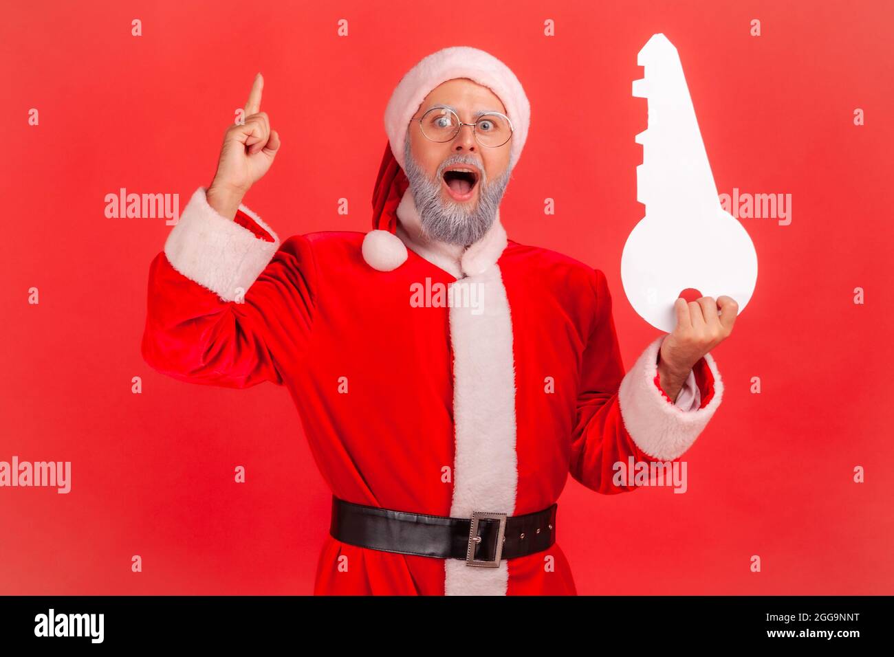 Porträt von staunenden älteren Mann mit grauem Bart trägt weihnachtsmann Kostüm stehen mit offenem Mund, hält Papierschlüssel, hat Idee für den Kauf von Immobilien. Stockfoto