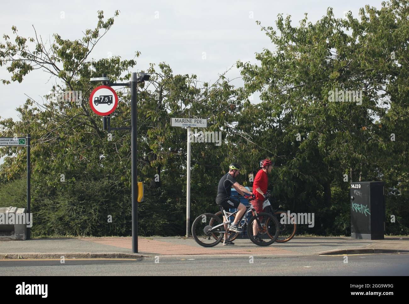 Zwei Radsportler mit Fahrradhelmen halten an, bevor sie die Straße bei der Marine Parade, Leigh-on-Sea, Essex, Großbritannien, überqueren Stockfoto