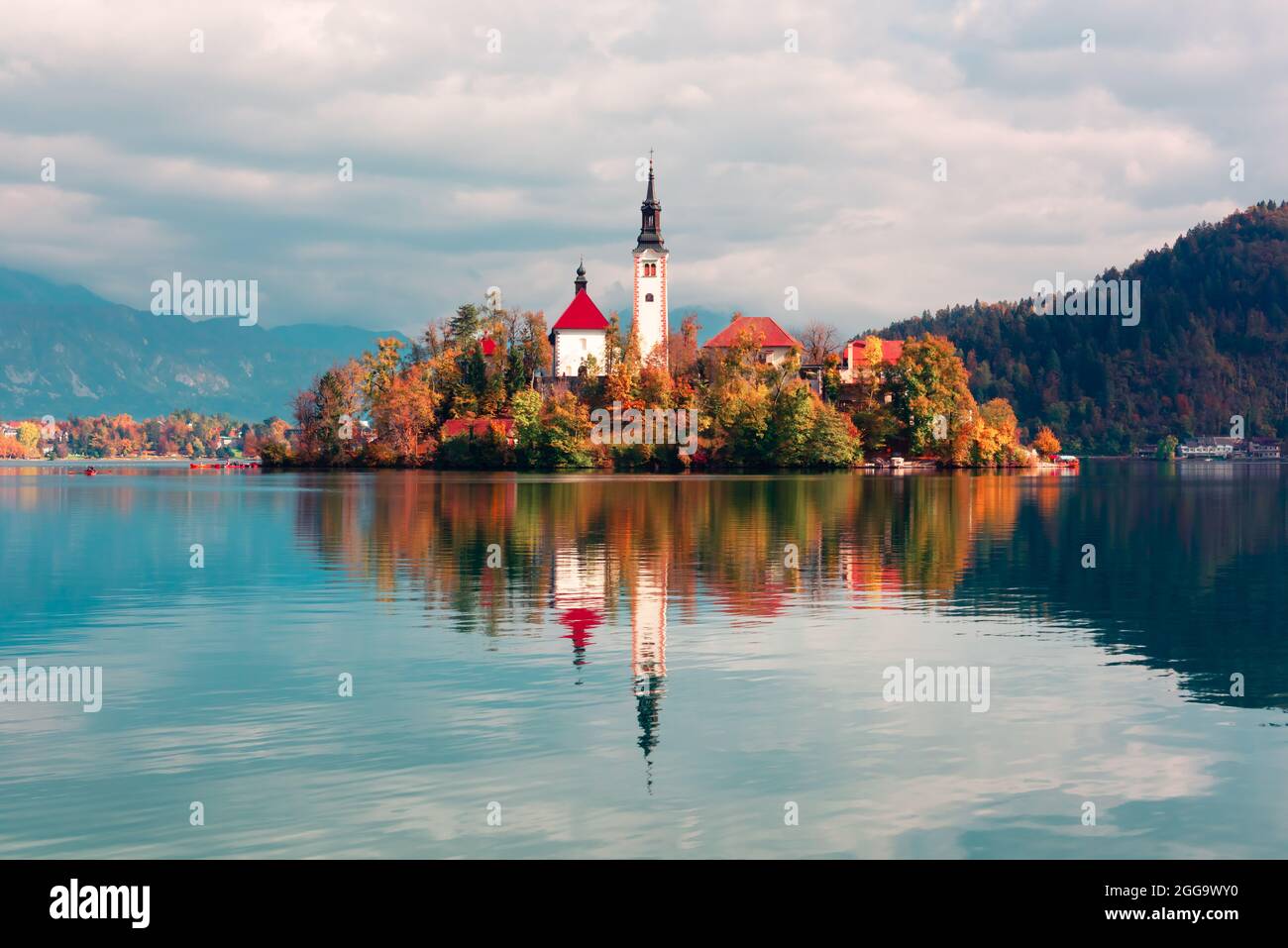 Bunte Herbst Blick auf See von Bled in den Julischen Alpen, Slowenien. Wallfahrtskirche der Himmelfahrt der Maria im Vordergrund. Landschaftsfotografie Stockfoto
