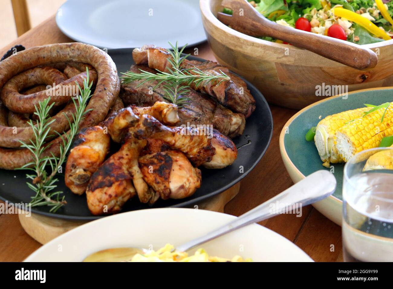 Grillen Sie Fleisch, Huhn und Boerewors auf Teller, fertig zum Essen mit Salat und Mais Stockfoto