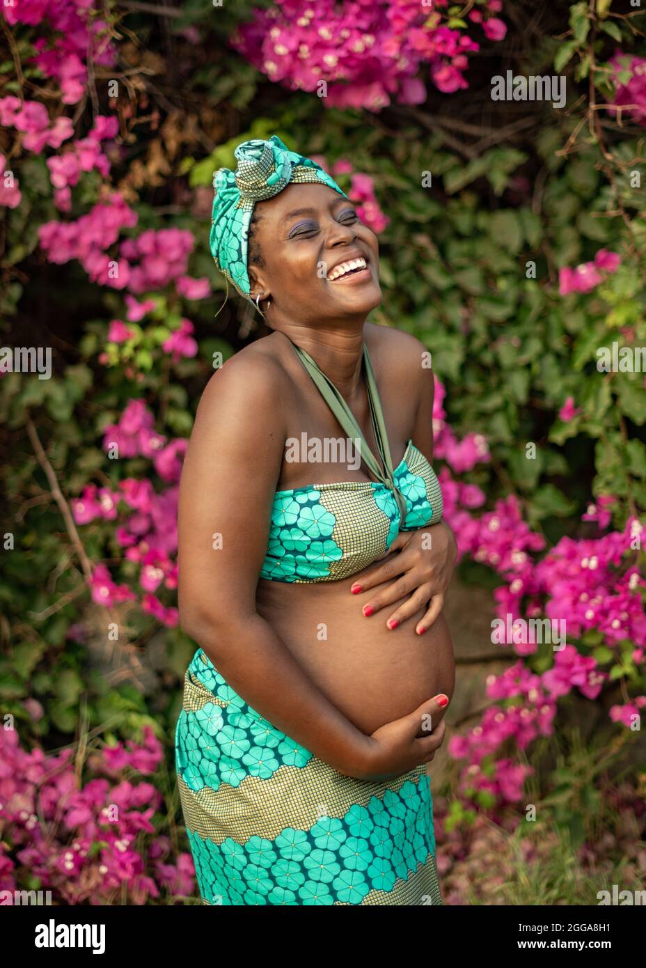 Glückliche, schwanger afrikanische Frau in der Nähe von blühenden Busch Stockfoto