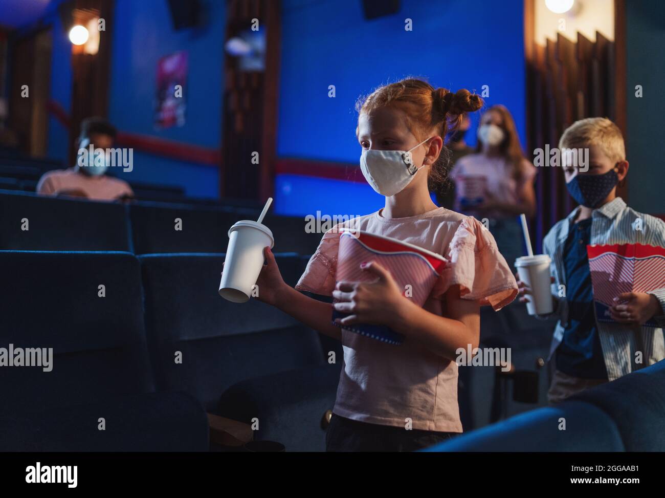 Glückliche kleine Kinder mit Popcorn zu Fuß im Kino, Coronavirus-Konzept. Stockfoto