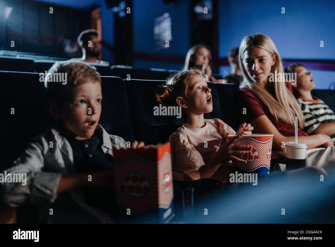 Mutter mit glücklichen kleinen Kindern im Kino, beim Film. Stockfoto