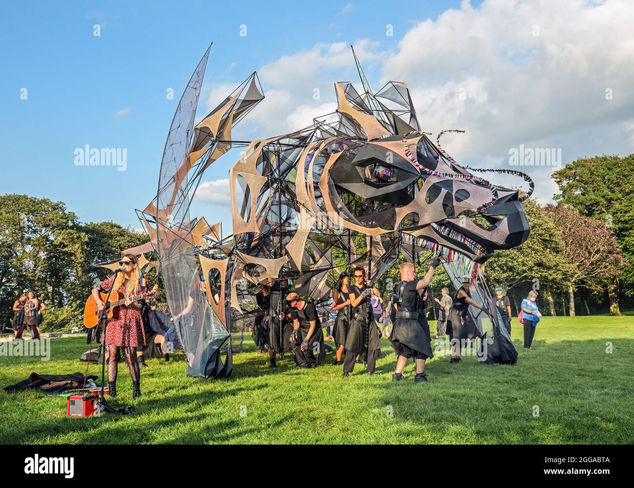 Unpreturbed by the Hatchling, a gigantic Dragon Puppet, a Singer on Plymouth Hoe setzt mit hr-Auftritt fort. Die Hatchling ist eine riesige Marionette und st Stockfoto