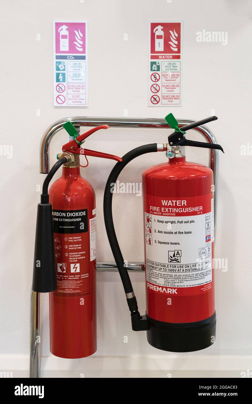 Ein Paar rote Feuerlöscher - Wasser und Kohlendioxid - auf einem Stützgestell in einem Büro mit Sicherheitshinweisen/Schildern, Großbritannien Stockfoto