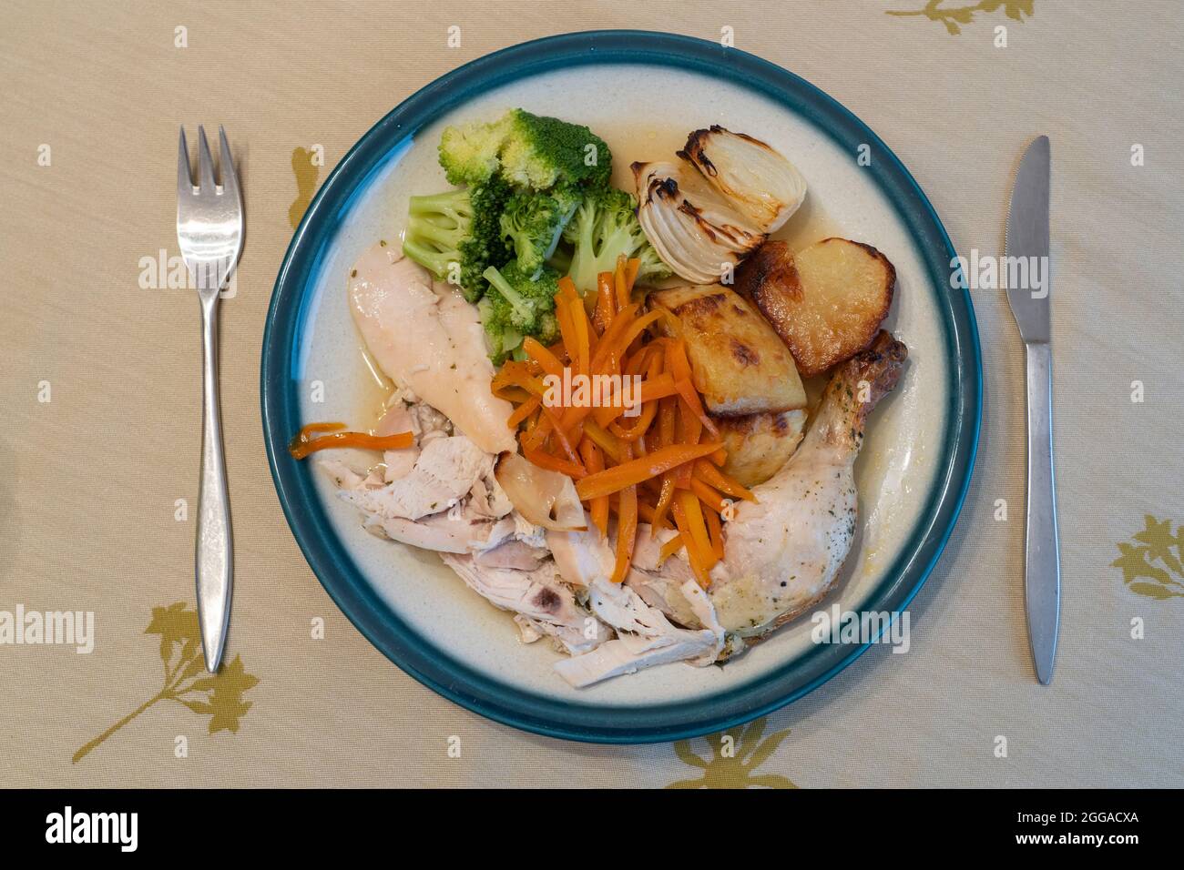 Ein vertikaler Blick auf ein typisch englisches Abendessen am Sonntag mit gebratenem Huhn, gebratenen Zwiebeln und Gemüse auf einem porzellanplatte mit Besteck Stockfoto