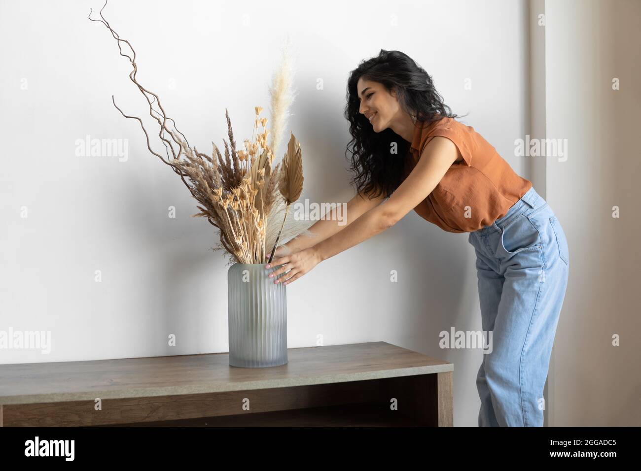 Modernes minimalistisches Innenraumdesign. Junge Frau arrangiert getrocknete Pflanzen in einer Vase und schafft eine gemütliche Atmosphäre im Haus Stockfoto
