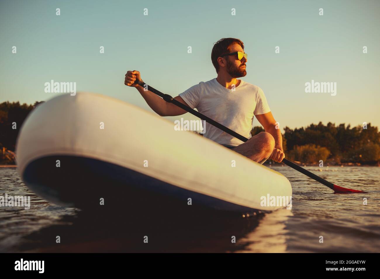 Hipster spaziert auf dem Boot am Sunset Lake. Paddle Boarder sitzt auf Paddleboards Stockfoto