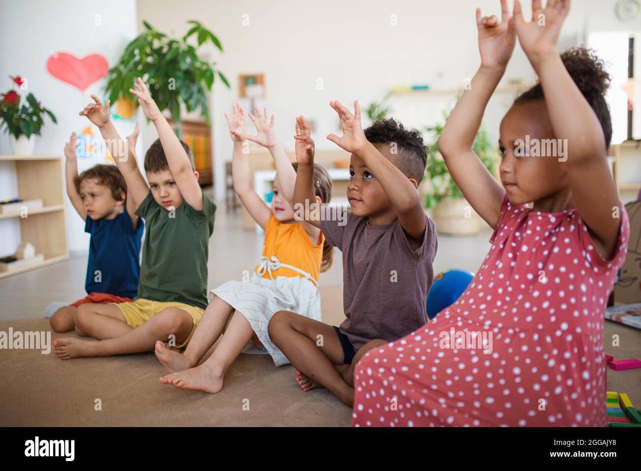 Gruppe von kleinen Kindergartenkindern, die im Klassenzimmer auf dem Boden sitzen und spielen. Stockfoto