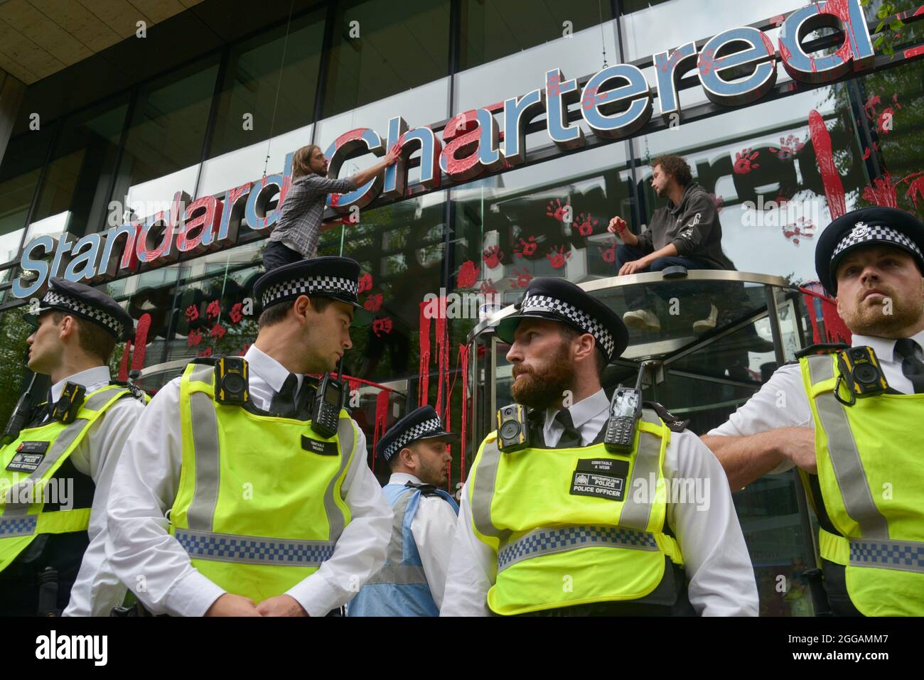 Die Polizei der Stadt London vor der Standard Chartered Bank, wo Umweltaktivisten rote Farbe an den Eingang der Bank warfen und Handmarken hinterließen Stockfoto