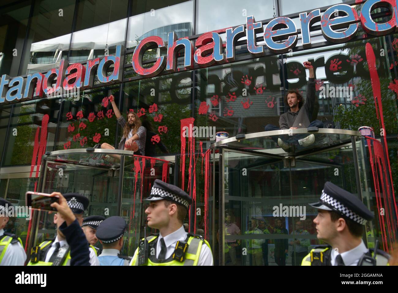Die Polizei der Stadt London vor der Standard Chartered Bank, wo Umweltaktivisten rote Farbe an den Eingang der Bank warfen und Handmarken hinterließen Stockfoto