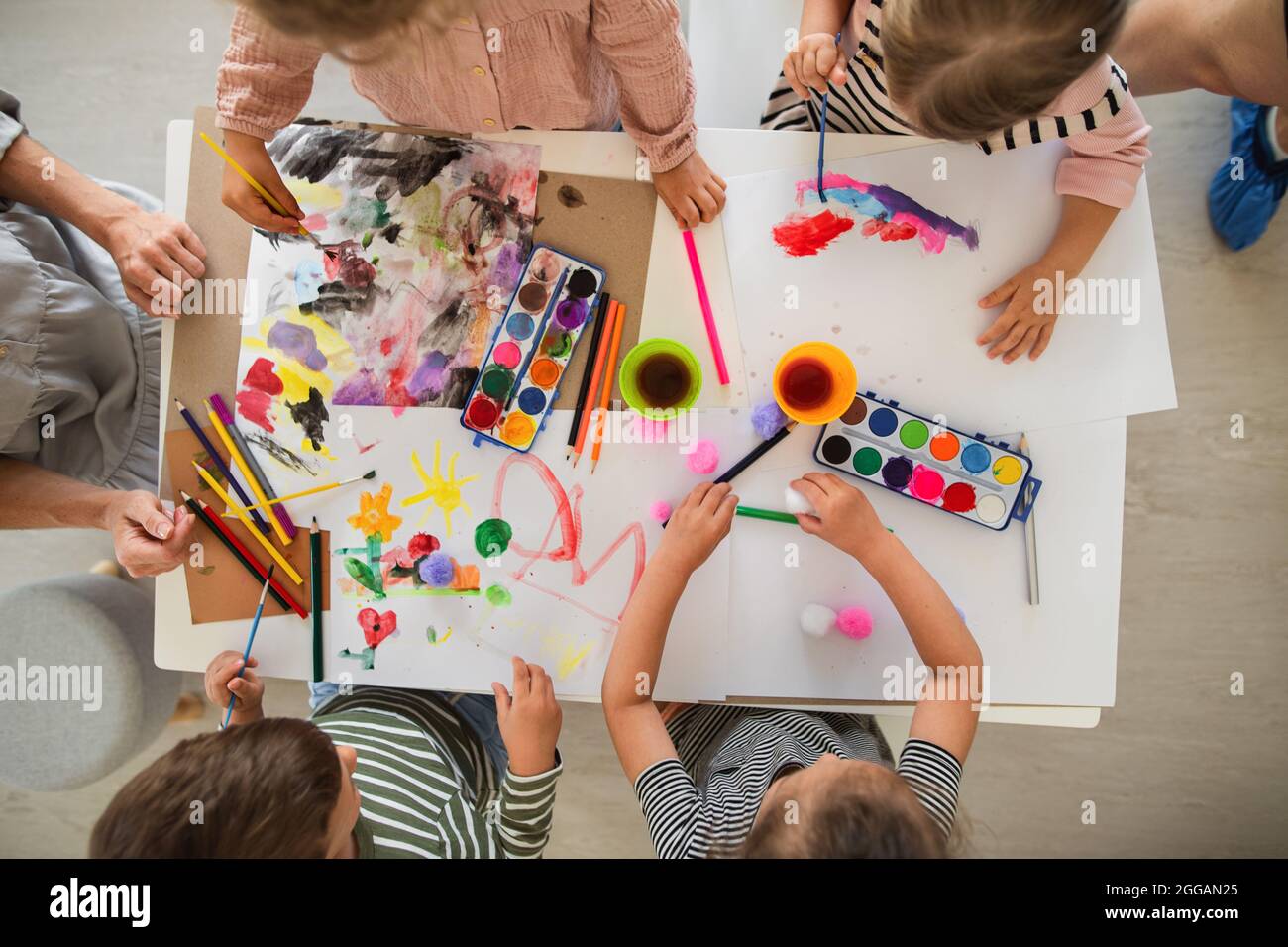 Draufsicht auf Gruppe von kleinen Kindergartenkindern mit Lehrer im Klassenzimmer, Malerei. Stockfoto